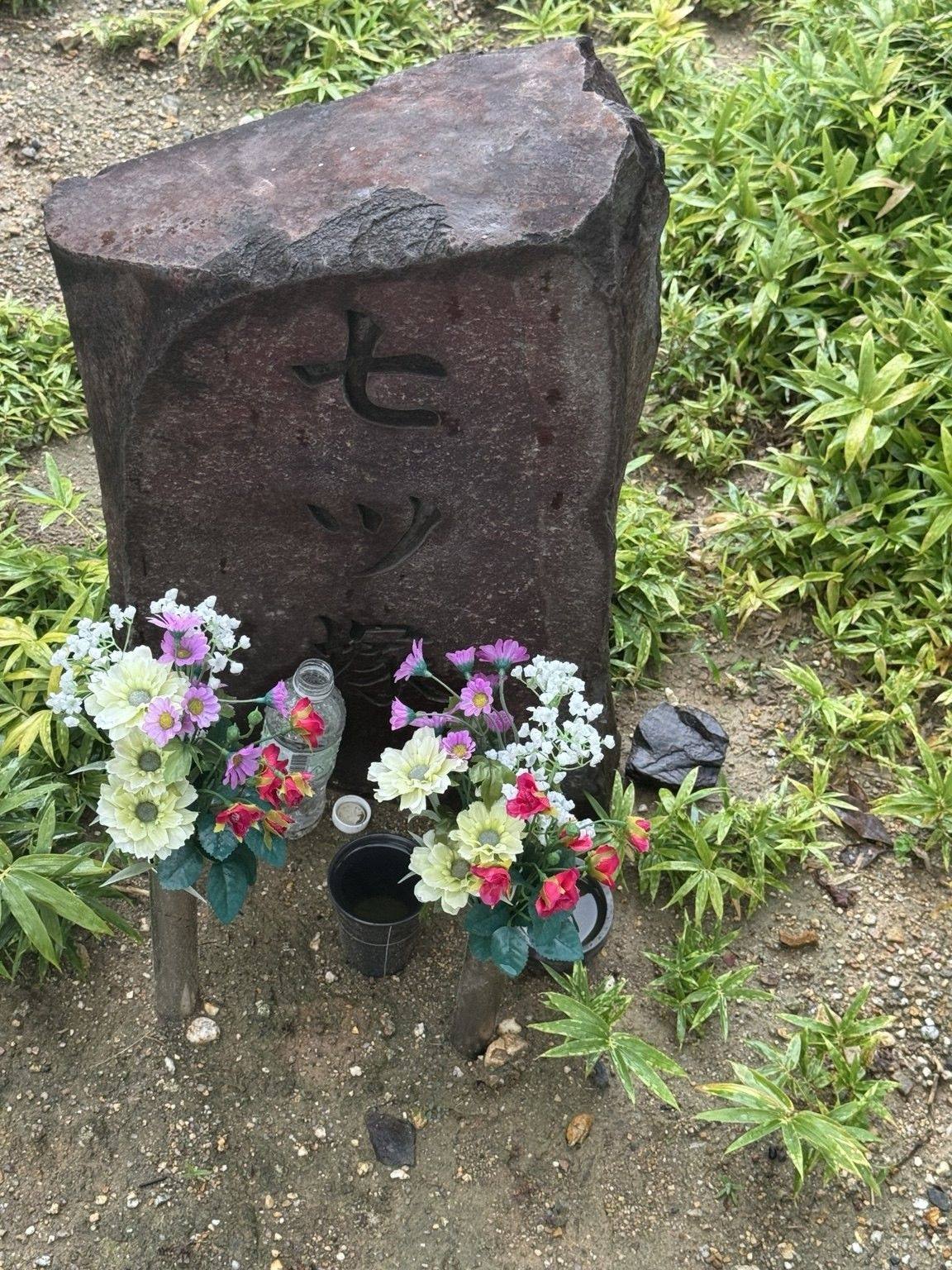 A carved stone marker for Nanatsuzuka with offerings of flowers