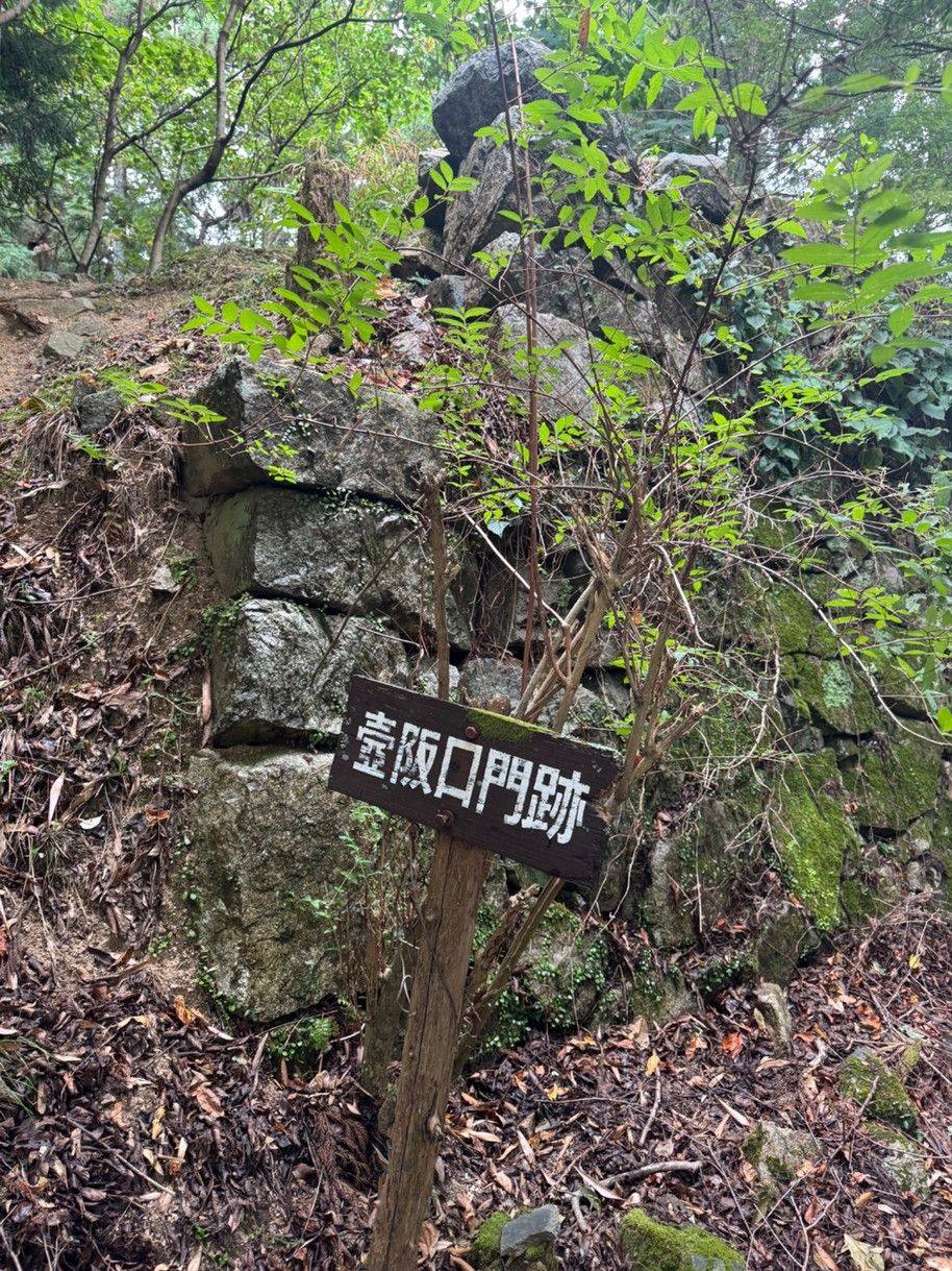 Overgrown stone walls and a sign marking the Tsubosakaguchi gate ruins